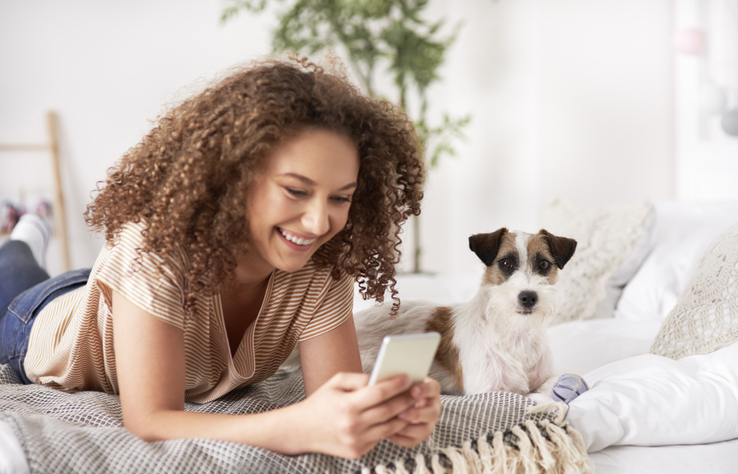 young girl scrolling through phone with puppy laying beside her