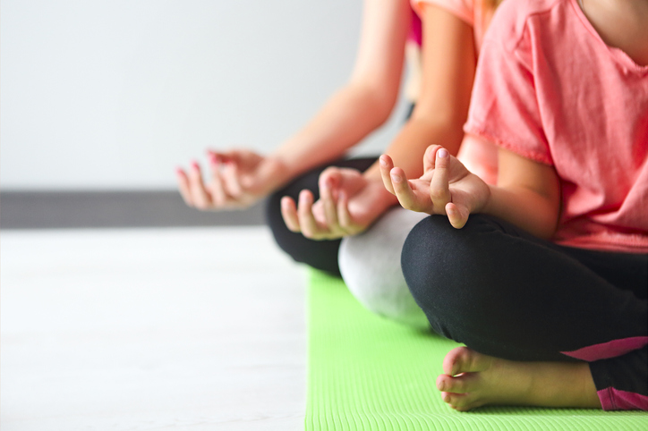 3 people meditating in a close up shot wearing bright colors and on a green yoga mat 