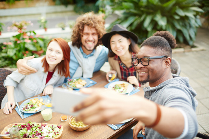 group of friends taking a selfie while enjoying some good food they are all smiling staring at the phone for a picture. 