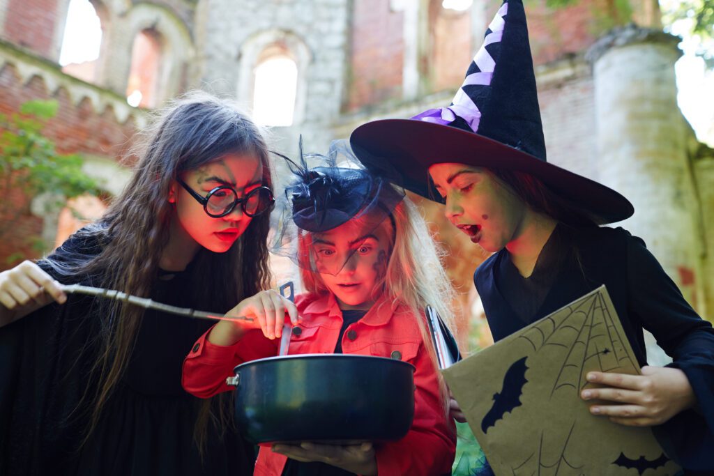 3 girls dressed in Halloween costumes looking into a bowl.