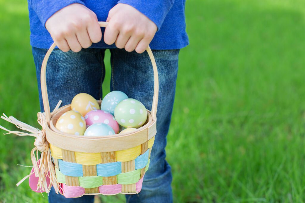 little boy with no face visible holding basket full of colorful easter eggs standing on the grass in the park after egg hunt
